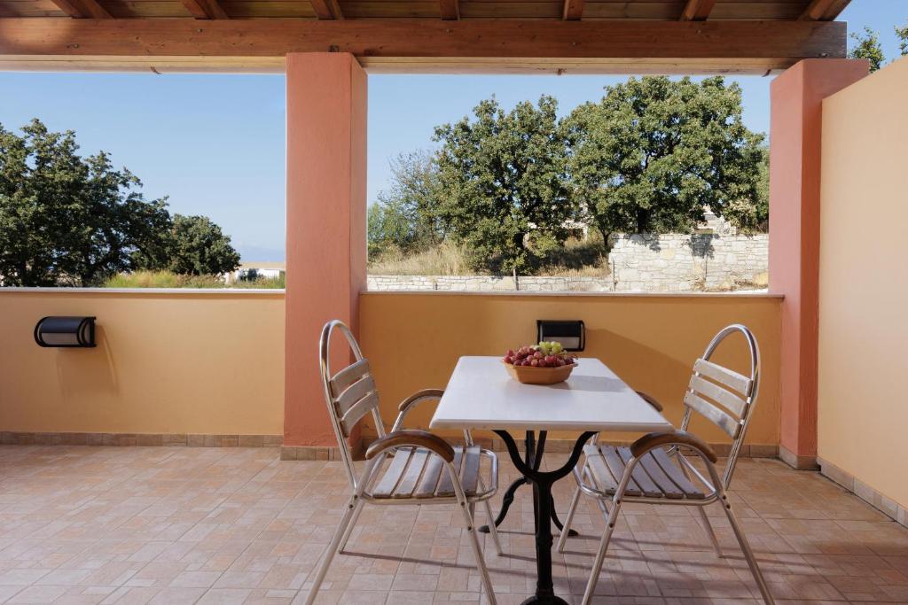 Terase ar galdu un krēsliem, kurā atrodas augļu bļoda, un fons ar kokiem un debesīm.