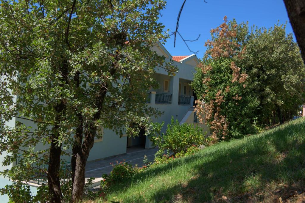 Mājas ar dārzu un kokiem, kas ieskauj ēku, radot mierīgu un dabisku atmosfēru. Skats uz gaišu fasādi un zilo debesu fona.