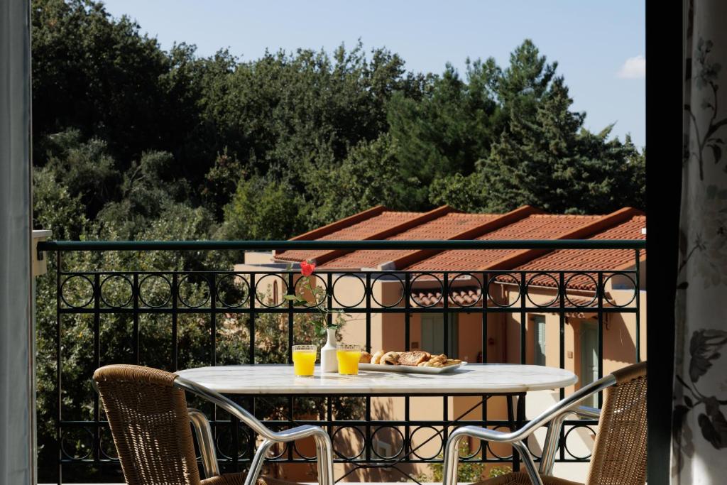Balcone ar galdu un krēslu, uz kura atrodas brokastis un dzērieni, ar skatu uz zaļo dārzu un ēkām ar sarkaniem jumtiem. Ideāla vieta relaksācijai un rīta baudīšanai.