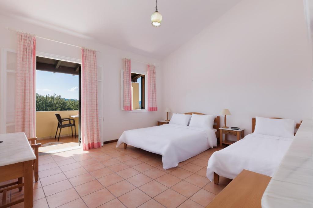 Gaiša un plaša guļamistaba ar divām gultām, koka mēbelēm un lieliem logiem, kas ved uz balkonu. Telpā ir siltas krāsas un vienkāršs dekors, radot mājīgu atmosfēru.