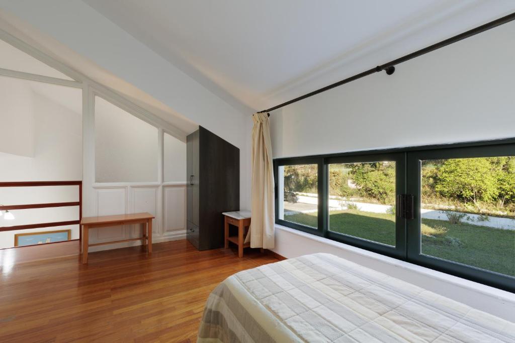 Mūsdienīga guļamistaba ar liela izmēra logiem, kas nodrošina dabisko apgaismojumu. Telpā ir koka grīda un minimālistiski mēbeļu elementi, radot mierīgu atmosfēru.