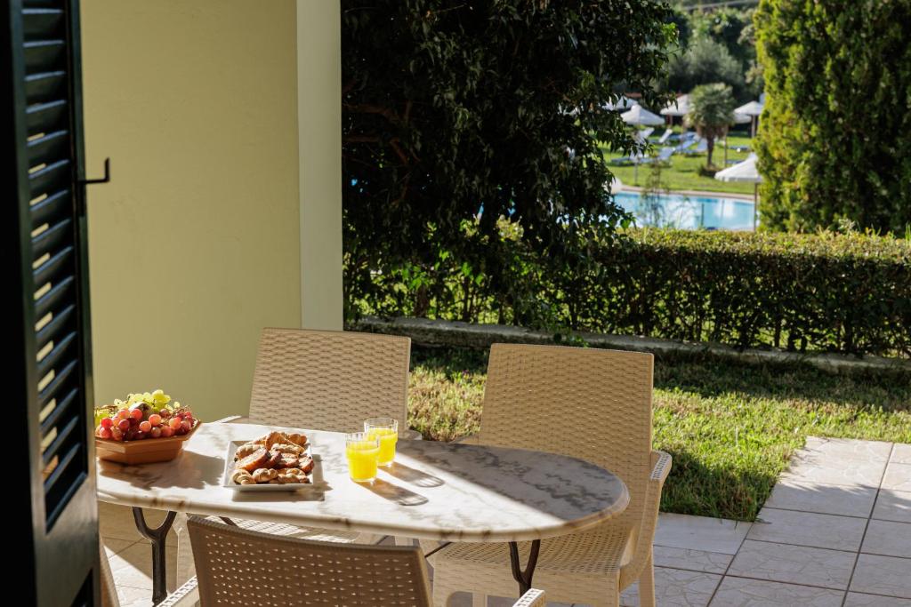 Terases zona ar galdu un krēsliem, uz galda ir augļi un dzērieni, skats uz peldbaseinu un ainavu.