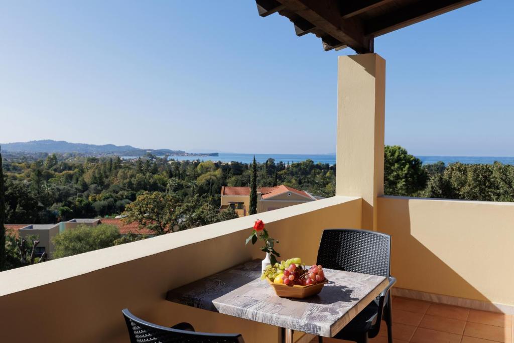 Skats no balkona uz jūru un ainavisku apkārtni, ar galdu, uz kura ir augļu bļoda un zieds.
