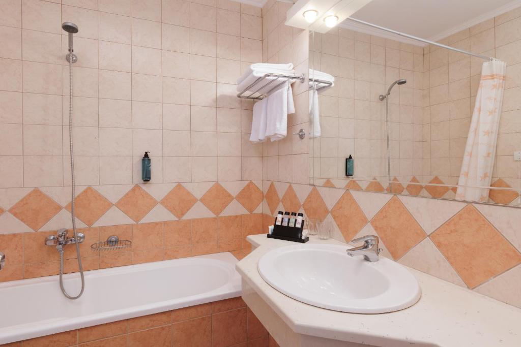 Vannas istaba ar vannu un dušu, apstrādāta ar gaišām flīzēm un elegantu dekora elementu, piemēram, higiēnas piederumiem un dvieļiem.