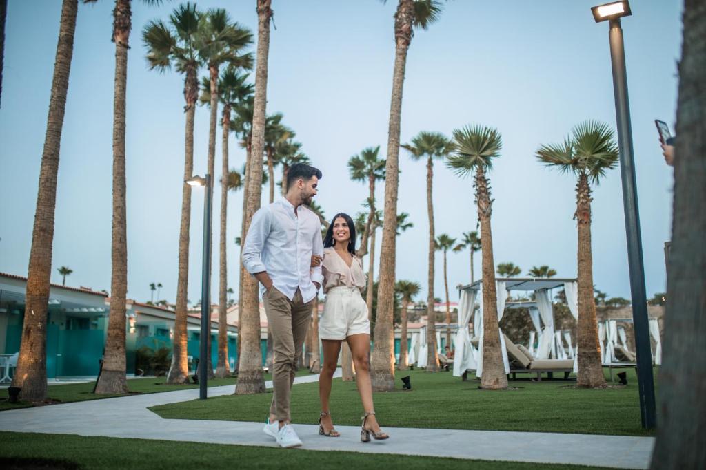 Pāris pastaigā pa modernu pludmales vidi, ko ieskauj palmas un elegantas gaismas. Ideāls brīvdienu mirklis romantiskā atmosfērā.