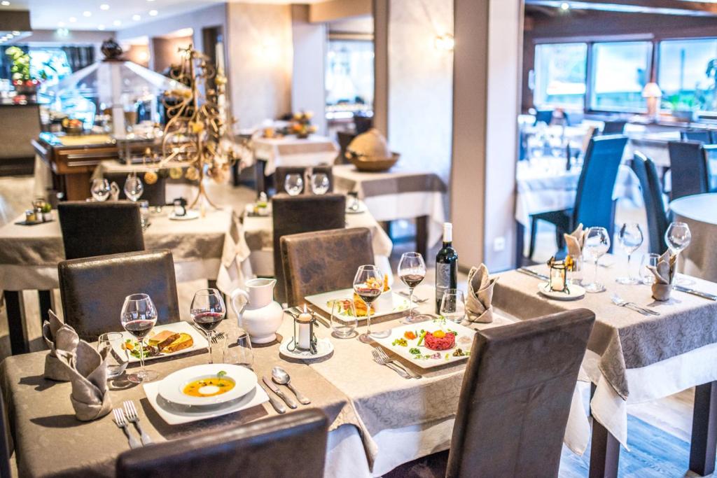 Elegantā restorāna interjers ar galds, kas klāts ar gourmet ēdieniem un vīnu. Rūpīgi noformēti galdi ar glāzēm un dekoratīvām servētēm rada patīkamu atmosfēru.