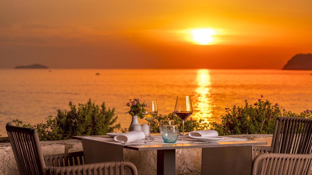 Romantisks saulriets pie jūras ar galdu, uz kura atrodas vīna glāzes un ziedi. Ideāla atmosfēra romantiskai vakariņai.