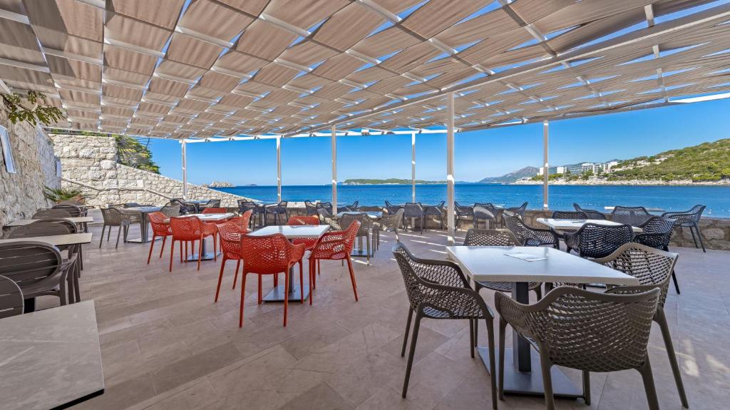 Mūsdienīga terase ar skatu uz jūru, kurā ir sarkanas un pelēkas krēsli, kā arī galdi, ideāli piemērota relaksācijai un ēdienreizei pie ūdens.