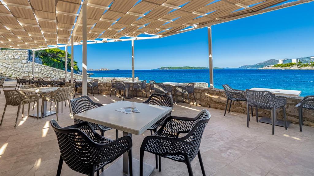 Restorāna terase ar skatu uz jūru, apkalpota ar modernām krēslām un galdiem. Gaisma un ēna veido patīkamu atmosfēru, ideāli piemērota relaksācijai.