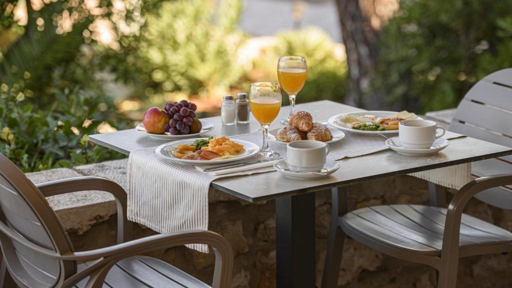 Broka ar izsmalcinātu brokastu komplektu, kas ietver augļus, maizes izstrādājumus un dzērienus, novietota uz galda zem atvērtā debesīm. Ideāla vieta rīta relaksācijai un baudīšanai.