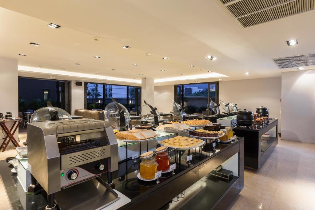 Bufete ar dažādiem ēdieniem un dzērieniem, iekārtota modernā vidē ar lielām logiem, kas nodrošina dabīgu apgaismojumu.