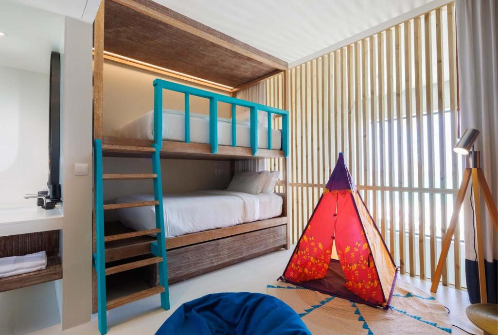 Mūsdienīga bērnu guļamistaba ar divstāvu gultu, spilgtu zilu detaļu un krāsainu telti rotaļām. Interjers ir gaišs un stilīgs, radot ērtu un priecīgu atmosfēru.