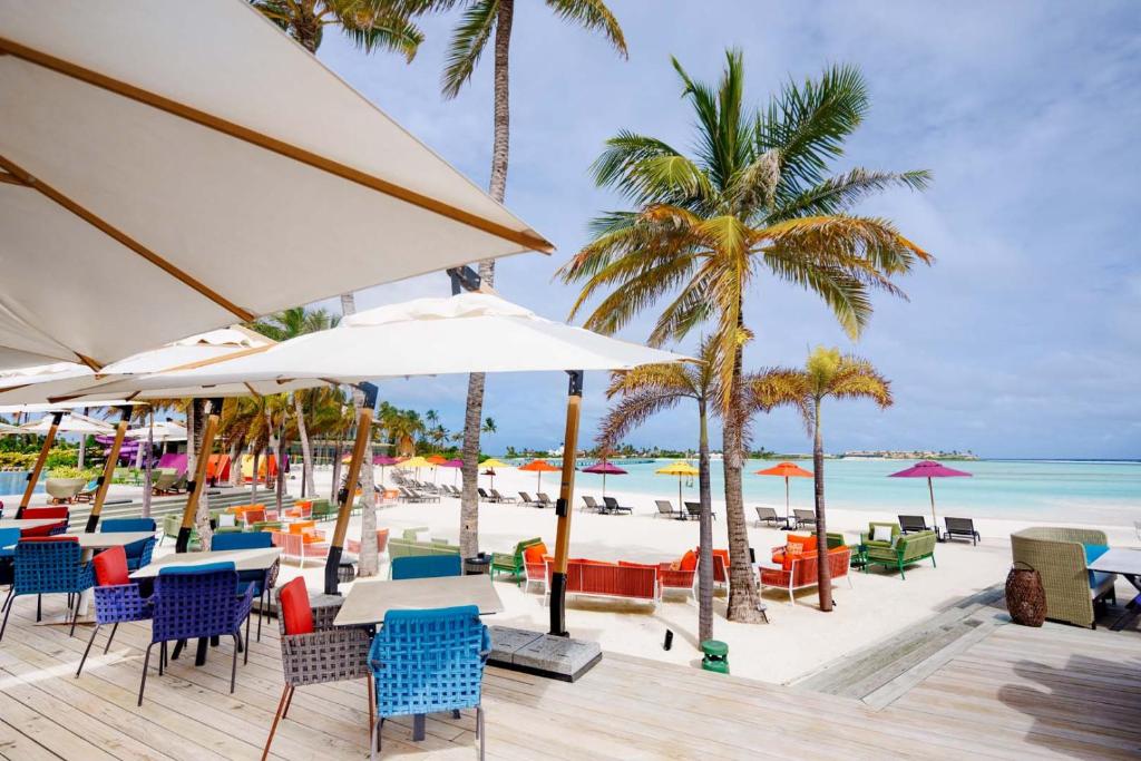 Krāšņs pludmales skats ar dzīvespriecīgām krāsainām mēbelēm, palmām un saulessargiem, kas radījuši relaksējošu atmosfēru. Ideāla vieta atpūtai pie jūras.