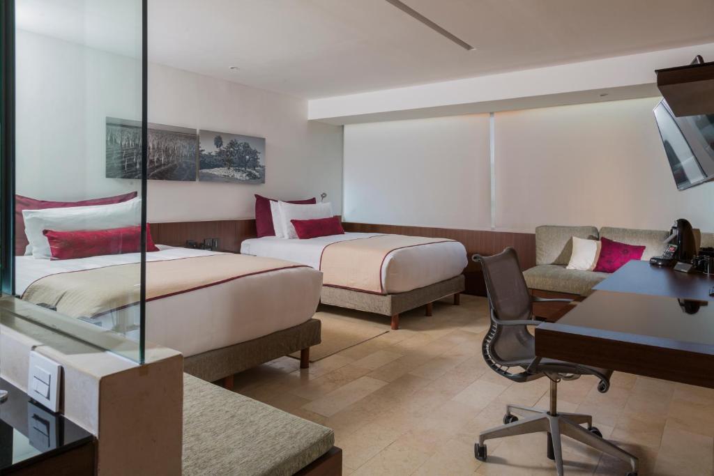 Mūsdienīgs viesnīcas numurs ar divām gultām, sēdvietu zonu un darba galdu. Telpa ir gaiša un ērta, ar moderniem interjera elementiem un ainavas attēliem uz sienām.