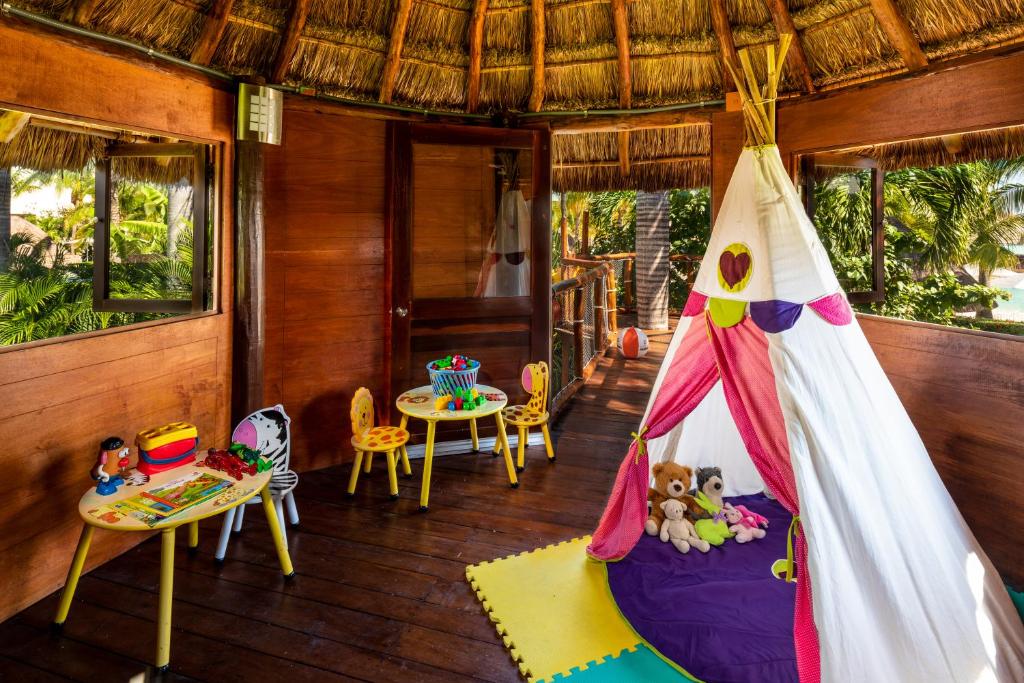 Bērnu rotaļu telpa ar dabīgu koka apdari, dekorēta ar krāsainu telšu, rotaļlietām un galdiņu. Telpā ir liels logs, kas paver skatu uz dabu.