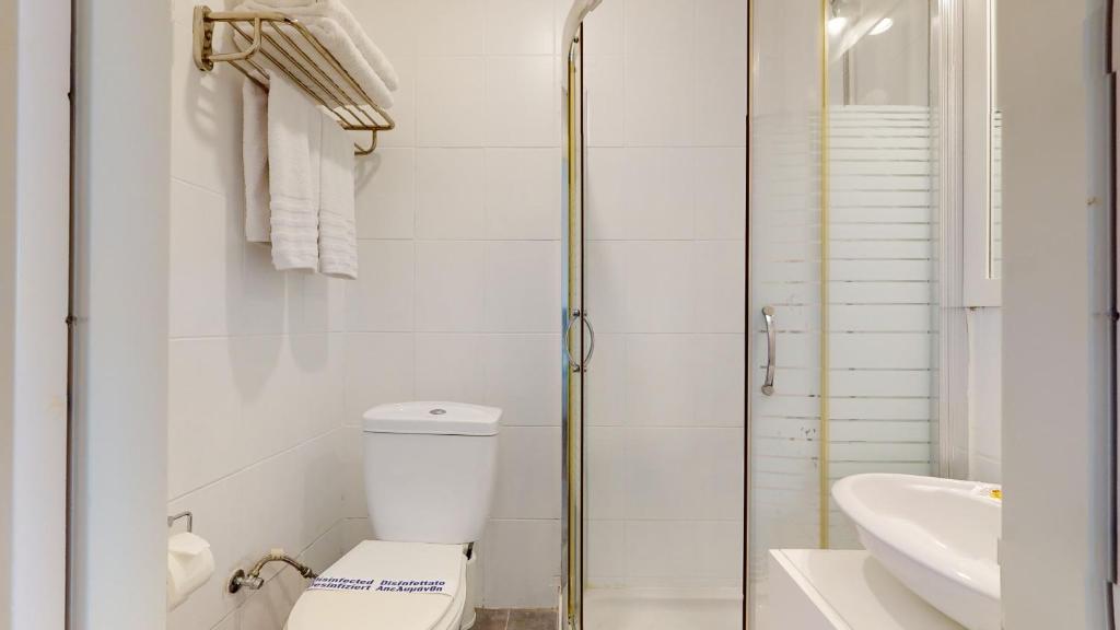 Mūsdienīga vannas istaba ar dušu, tualeti un baltām dvielēm, kas sakārtoti uz statīva. Interjers ir gaišs un tīrs, radot patīkamu atmosfēru.