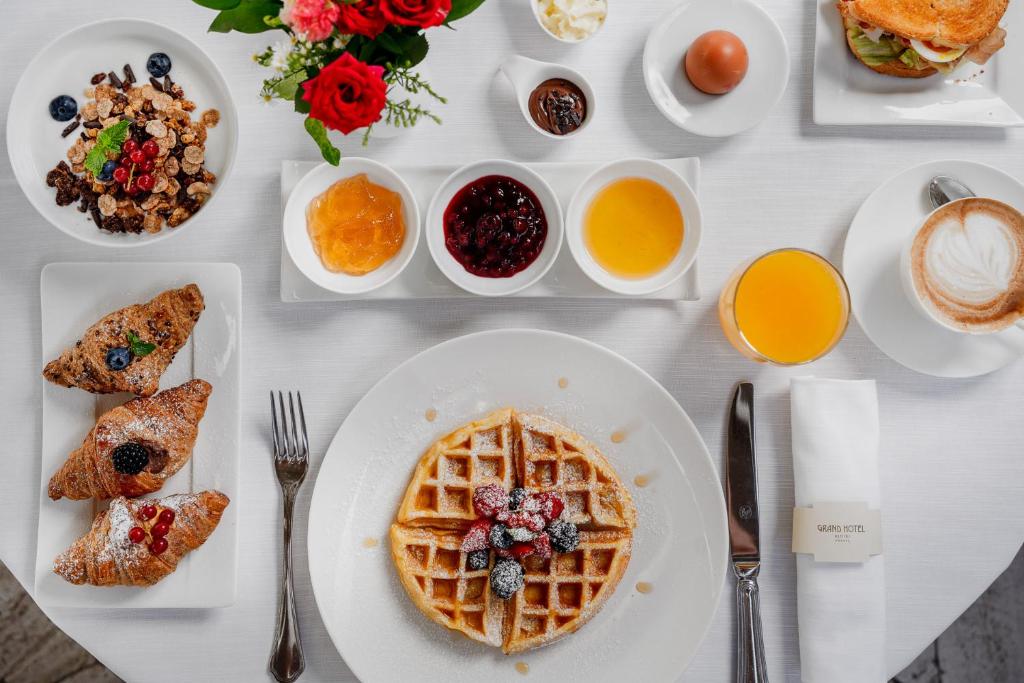 Brokastu galds ar vafelēm, kruasāniem, augļu ievārījumiem, jogurtu, kafiju un sulu. Uz galda ir arī graudaugi un ziedi.