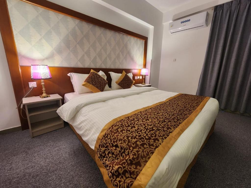 Mūsdienīgs guļamistabas interjers ar divguļamo gultu, dekoratīvām spilveniem un naktslampām, kas rada mājīgu atmosfēru. Telpā ir arī gaisa kondicionieris un aizkari, nodrošinot komfortu un privātumu.