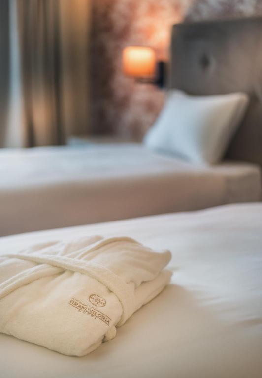 Viesnīcas numura gulta ar baltu halātu, kas novietots uz gultas. Fons ar mīkstām krāsām un apgaismojumu, radot relaksējošu atmosfēru.