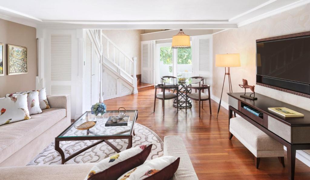 Mūsdienīgs viesistabas interjers ar gaišām krāsām, elegantu mēbelēm un koka grīdu. Telpā ir dīvāns ar spilveniem, stikla galdiņš un ērtas ēdināšanas vietas.