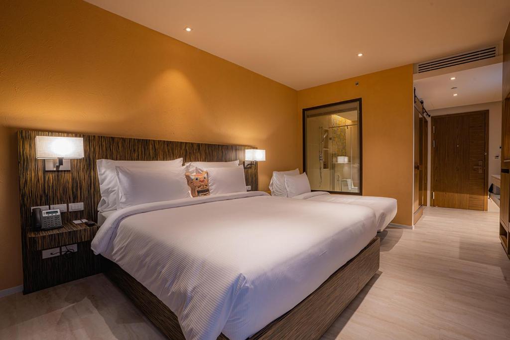 Mūsdienīga viesnīcas numura iekārtojums ar divām gultām, siltām krāsām un modernas apgaismojuma ierīcēm. Numurā ir arī vannas istaba ar stikla durvīm un ērtiem mēbelēm.