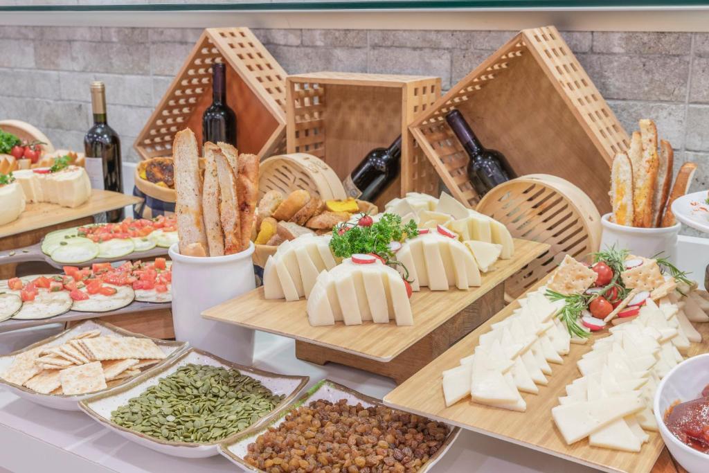 Svaigu sieru, maizes, dārzeņu un uzkodu klāsts ar sarkanvīna pudelēm un dekoratīvām koka groziem. Ideāla uzkodu izvēle svinībām vai pasākumiem.