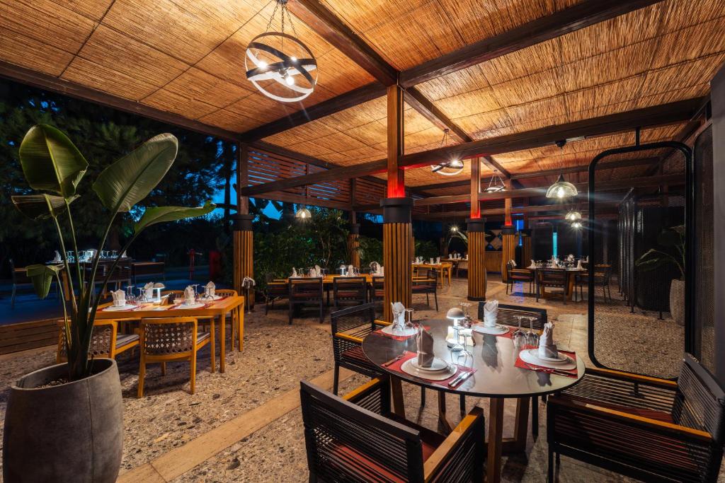 Mūsdienīga restorāna interjers ar elegantiem galdiem un krēsliem, kas apgaismots ar stilīgām lampām. Vides elementi, piemēram, augi un dabīgās materiālu tekstūras, rada patīkamu atmosfēru.