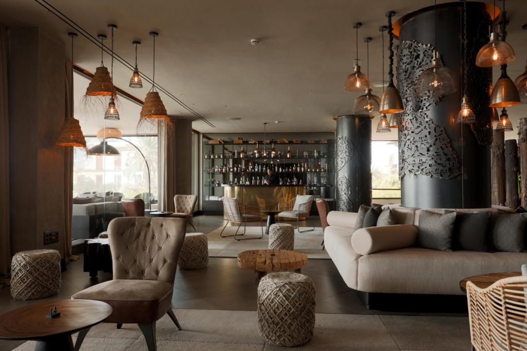 Mūsdienīgs viesnīcas bārs ar stilīgu interjeru, kas ietver komfortablu dīvānu, elegantu krēslu un dekoratīvas laternas. Atmosfēra ir silta un viesmīlīga, ideāli piemērota relaksācijai.