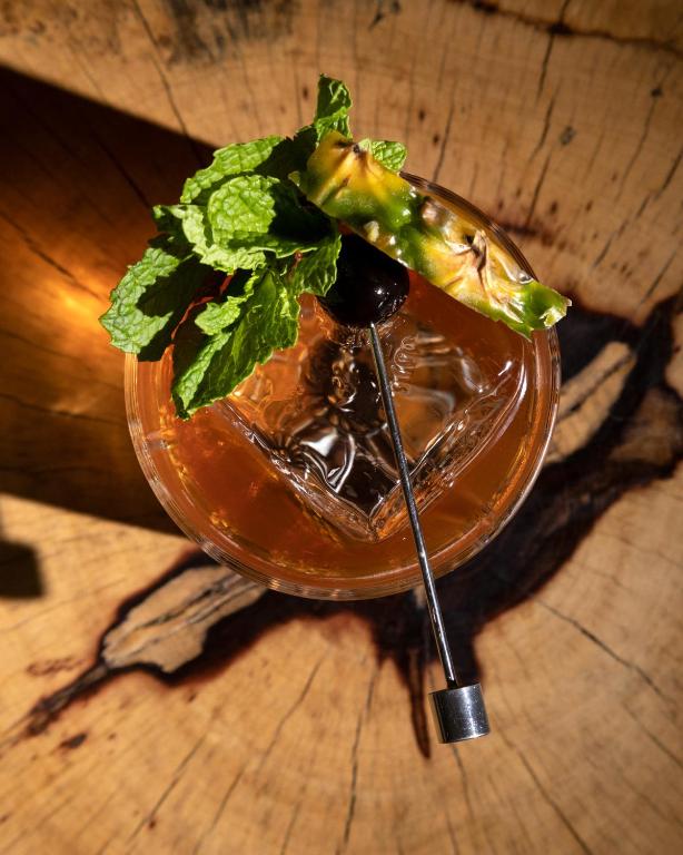 Margarita glāze ar ananāsu, piparmētru un ķiršu dekoru uz koka galda.