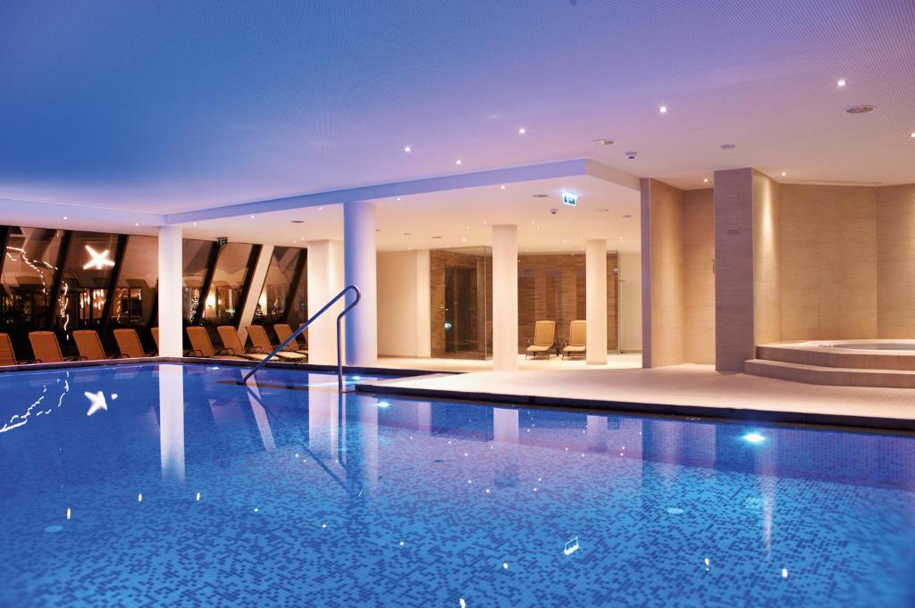 Moderns iekštelpu peldbaseins ar relaksācijas zonu, apgaismots ar maigu zilu gaismu. Viegla un eleganta atmosfēra, kas aicina uz atpūtu un relaksāciju.