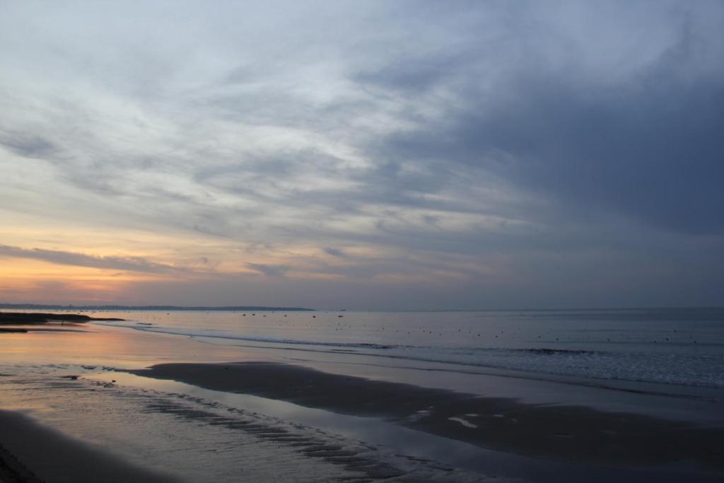 Saulrieta skats pie pludmales, kur jūra un debesis saplūst kopā, radot mierīgu un maigu atmosfēru. Gaisma un krāsas atspoguļojas ūdenī, veidojot gleznainu ainavu.