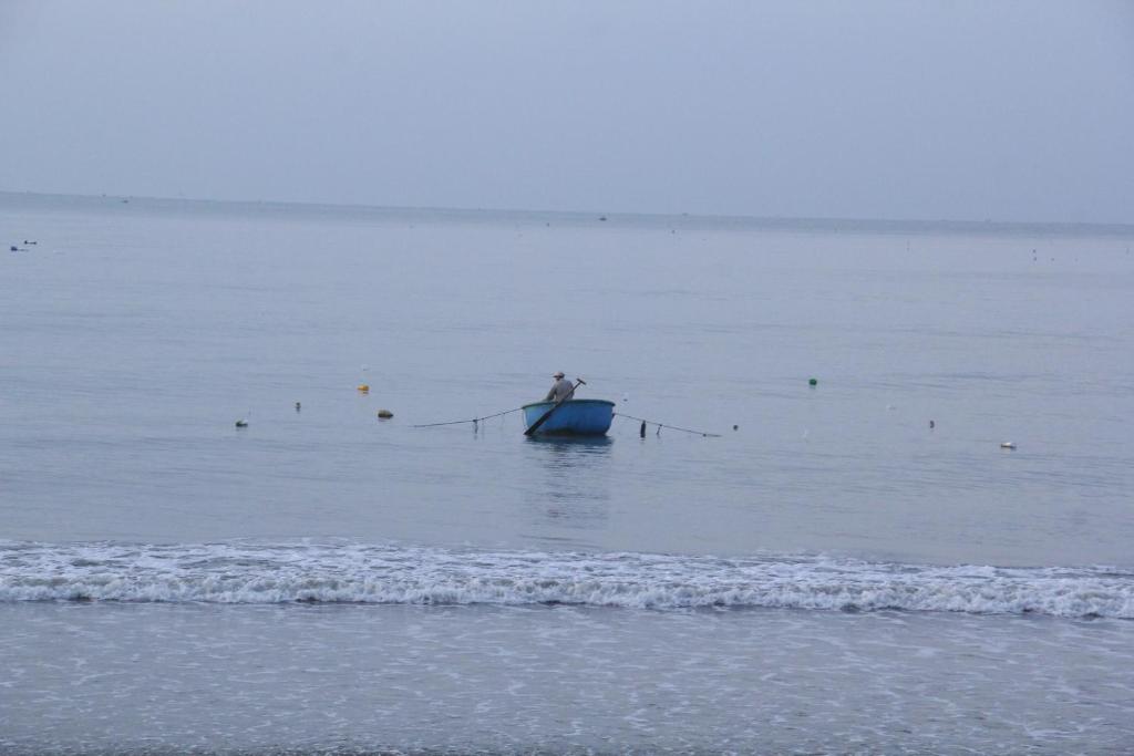 Zvejnieks laivā mierīgā jūrā, apkārt peldot zvejas piederumiem. Jūrmala izskatās apmākusies un klusa.