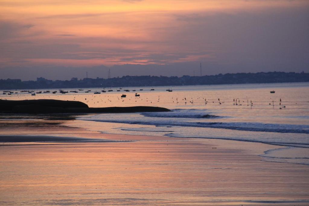Saulrieta ainava pie jūras ar maziem kuģiem un mierīgu ūdeni, kas atspoguļo debesu krāsas. Klusa pludmale, kas iemūžina vakara burvību.