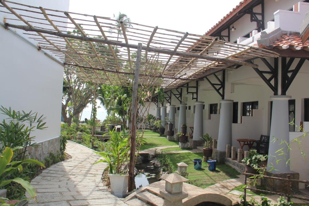 Dabas viesnīcas pagalms ar akmens ceļu un zaļumiem, kas ved uz pludmali. Skats uz ēkām ar koka konstrukciju un atpūtas zonām.