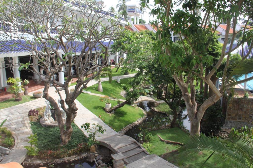 Skaists dārzs ar izveidotiem celiņiem, zaļām zālēm un kokiem, kas rada mierīgu un relaksējošu noskaņu. Dārzā redzami arī dekoratīvie elementi un ūdens plūsmu.