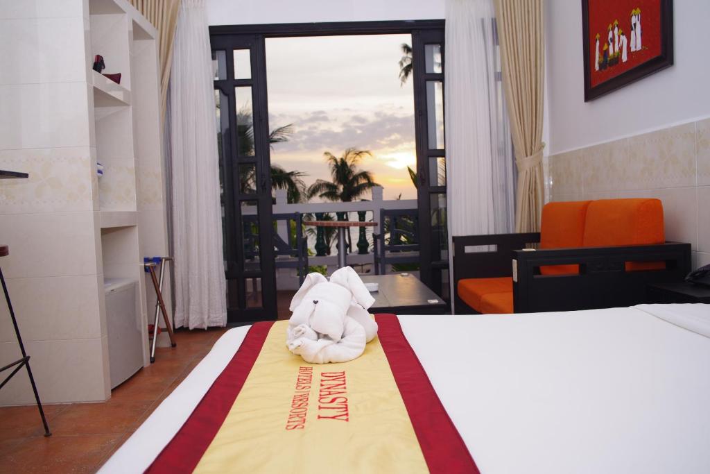 Mūsdienīga viesnīcas numura iekārtojums ar skatu uz saulrietu, kurā redzama gultas veļas kompozīcija un oranža dīvāna stūris.