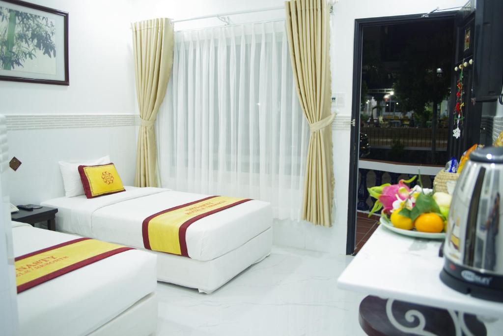 Mūsdienīgs viesnīcas numurs ar divām gultām, gaišām aizkariem un telpu, kas paveras uz ārpusi. Uz galda novietoti augļi un tējkanna, radot mājīgu atmosfēru.