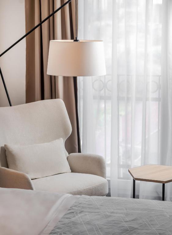 Mūsdienīgs un elegants viesnīcas interjers ar pelēku krēslu, galdiņu un mīkstu apgaismojumu. Logi ar gaismas aizkariem rada mājīgu atmosfēru.