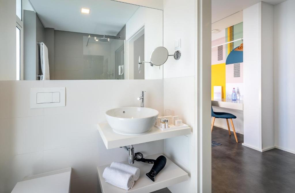 Moderns vannas istabas interjers ar elegantu izlietni un spoguli, kas atrodas blakus gaišai telpai ar krāsainām sienām. Tajā ir arī higiēnas piederumi un matu fēns.