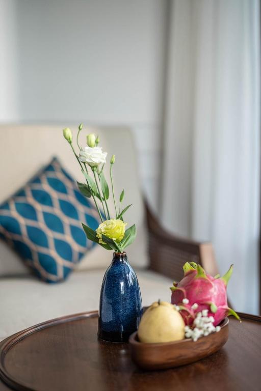 Zilā vāzē ir ziedi, bet uz galda ir augļi, tostarp drakona auglis un bumbieris. Fons veido mājīgu interjeru ar dīvānu un spilvenu.