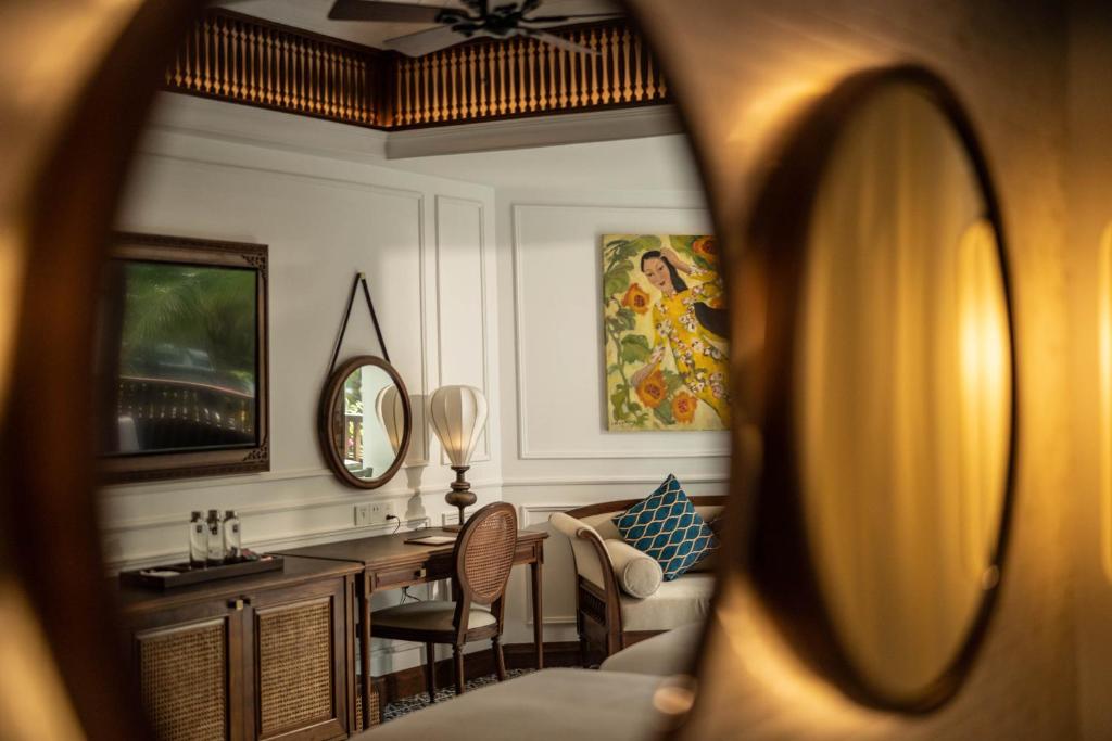 Eleganta viesnīcas numura interjers ar atspoguļotu spoguli, koka mēbelēm un krāsainu gleznu uz sienas. Mīksta dīvāna un rakstāmgalda kombinācija rada mājīgu atmosfēru.