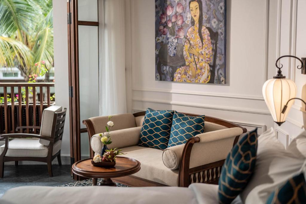 Mūsdienīgs viesistabas interjers ar elegantu dīvānu, dekoratīviem spilveniem un mākslas darbu uz sienas. Logi atveras uz zaļu terasi, radot mājīgu un relaksējošu atmosfēru.