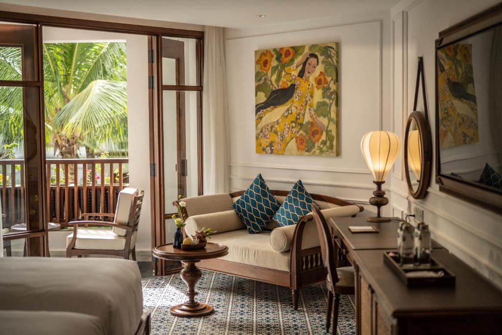 Mūsdienīga viesnīcas numura interjers ar ērtu dīvānu un mākslas darbu uz sienas, kurā redzami saulaini ziedi. Logi nodrošina gaismas plūsmu un skatu uz zaļo dārzu.