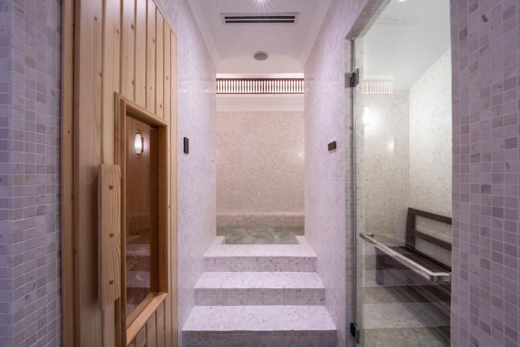 Mūsdienīga sauna ar koka durvīm un mozaīku apdari, kas aicina uz relaksāciju un atpūtu. Telpā ir skaidri redzamas pakāpieni un stikla durvis, kas piešķir gaisīgu izskatu.