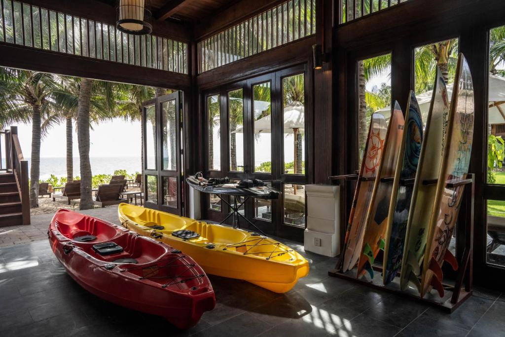 Telpa ar sarkaniem un dzelteniem kajakiem, kā arī sērfošanas dēļiem, kas novietoti blakus lieliem logiem, caur kuriem redzama jūra un palmas.