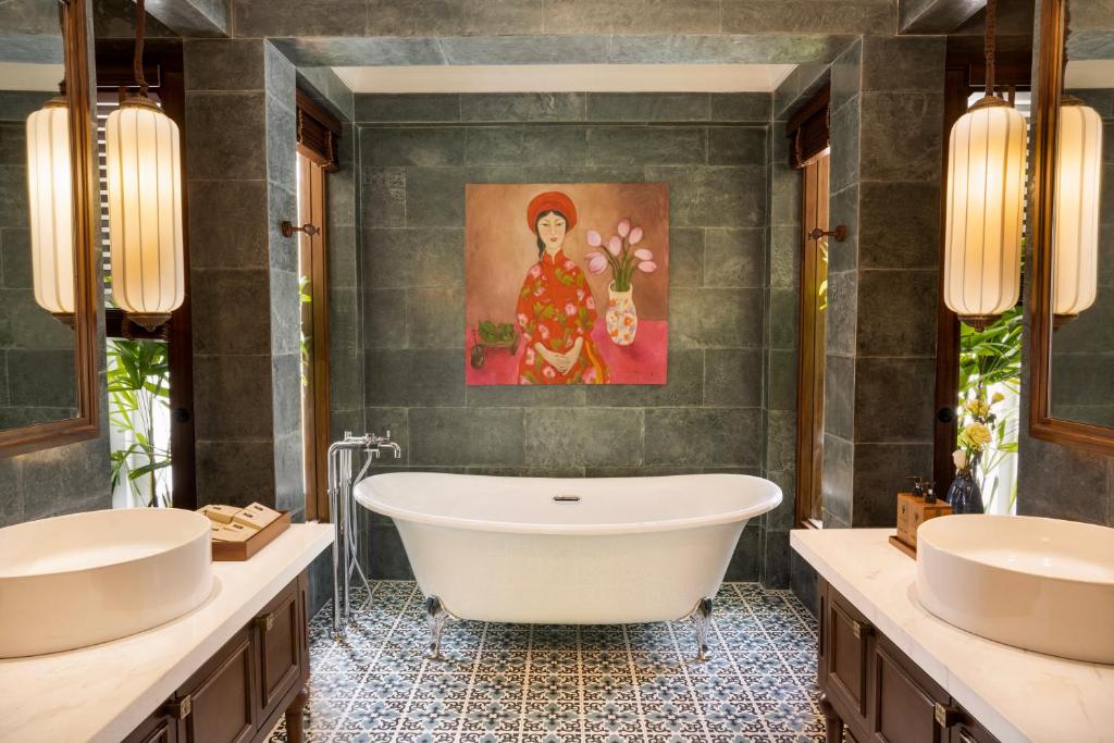 Elegants vannas istabas interjers ar brīvi stāvošu vannu un mākslas darbu pie sienas. Ir redzami dabiski elementi un stilīgas gaismas ķermeņi.