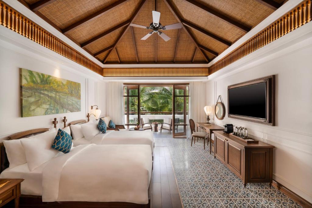 Mūsdienīga viesnīcas numura interjers ar divām gultām, koka griestiem un lieliem logiem, kas ved uz terasi ar skatu uz dārzu. Numurā atrodas televizors, galds un krēsli, kā arī mākslas darbs uz sienas.