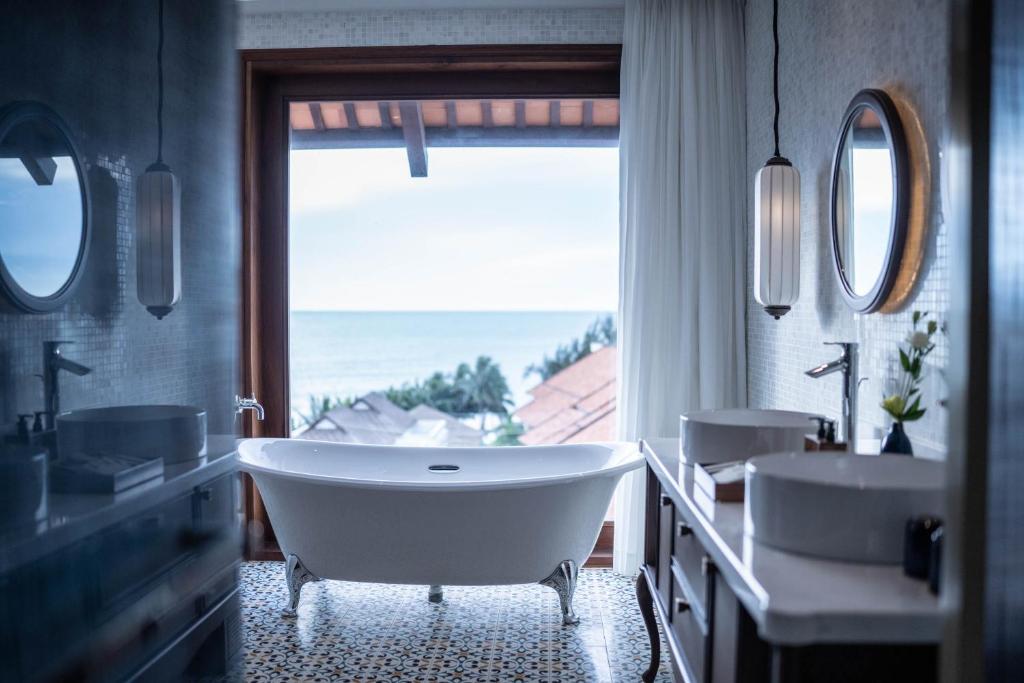 Mūsdienīga vannas istaba ar brīvdabas skatu uz okeānu, kurā ir eleganta brīvi stāvoša vanna un modernas izlietnes. Stils apvieno komfortu un estētiku, radot relaksējošu atmosfēru.