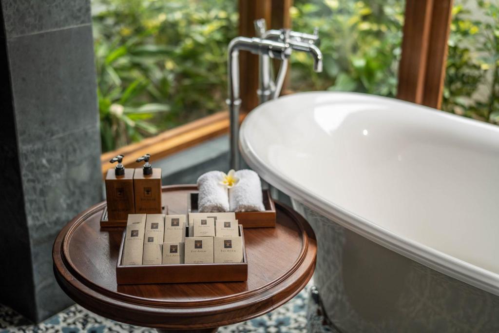Luksusa vannas istaba ar elegantu vannu, koka galdu, uz kura novietoti higiēnas līdzekļi un dvieļi, ar zaļo dabu fonā.