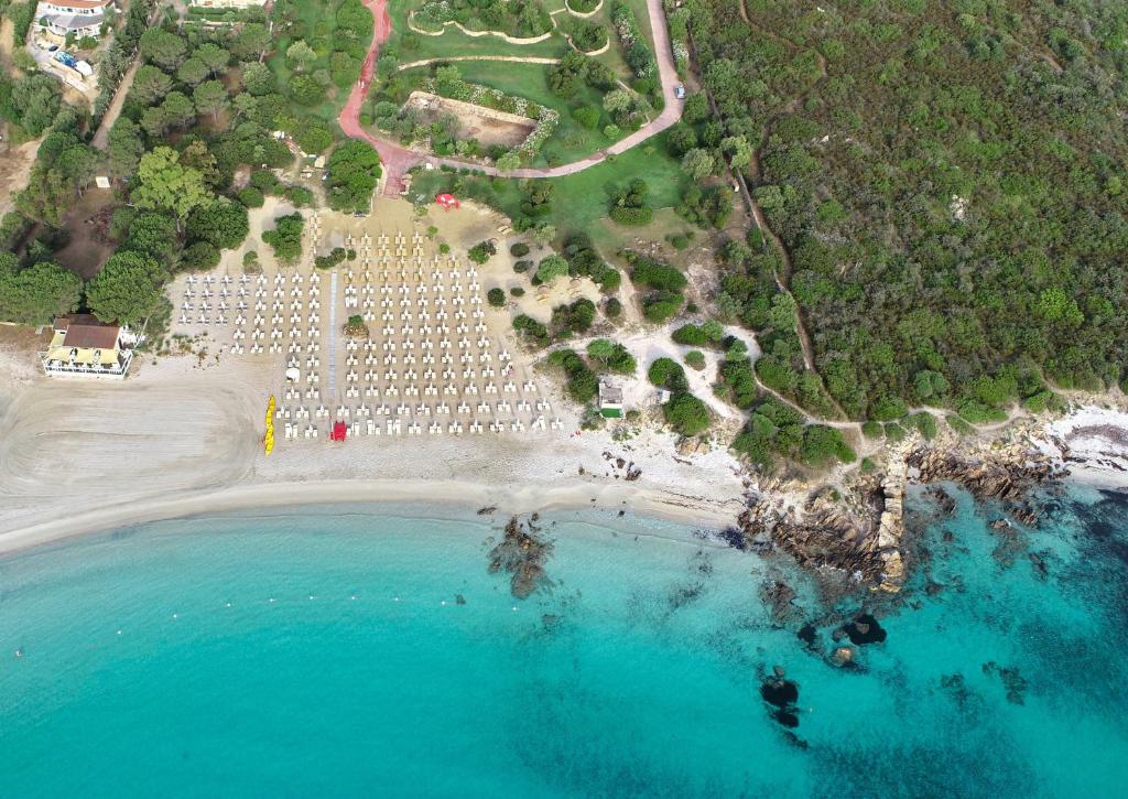 Pludmale ar saulessargiem un šūpuļtīkliem, kas izvietoti uz smilšu krasta, blakus zilam ūdenim un zaļiem kokiem. Skats no augšas uz pludmali un apkārtējo dabu.